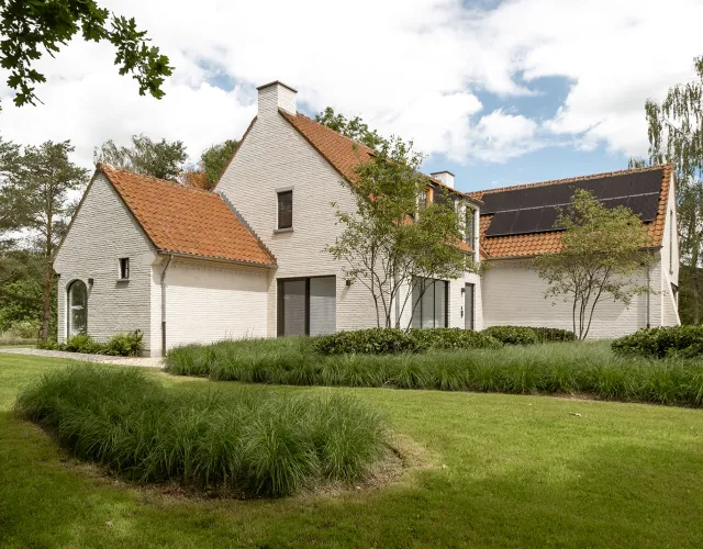 Witgekaleide hoevestijl villa met zonnepanelen, omringd door glooiend gazon en siergrassen