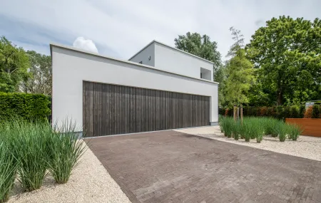 Voorgevel modern wit huis met houten poort en moderne tuin. 