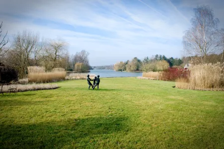 Groene tuin met aanplanting en kunstwerk, uitzicht op meer. 