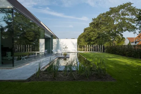 Villa met grote raampartijen reflecterend in zwemvijver. 