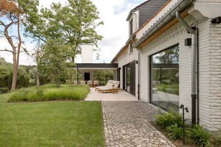 Overdekt terras met loungezetels naast de witgekaleide villa en kasseipad