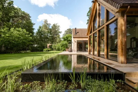 Zwemvijver met rietplanten tegen de glazen gevel van de houten villa in Bonheiden