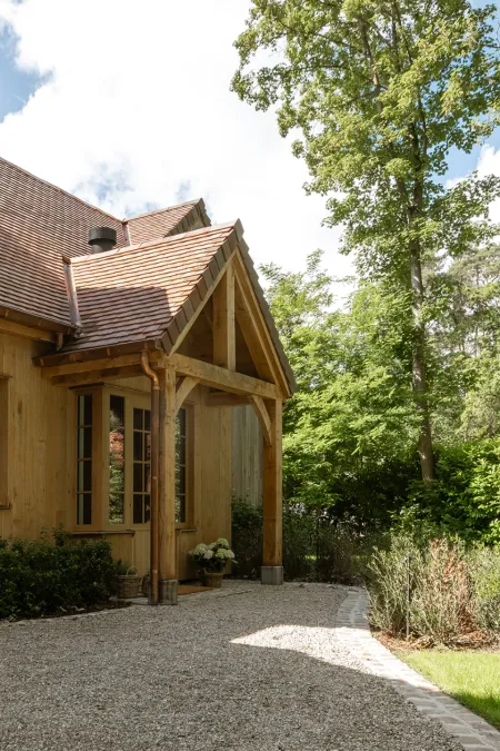 Houten veranda met balkenconstructie en grindpad naar de houten villa in Bonheiden