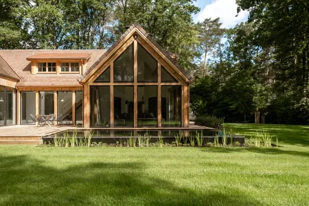 Glazen puntgevel van de houten villa met zwemvijver ervoor in Bonheiden