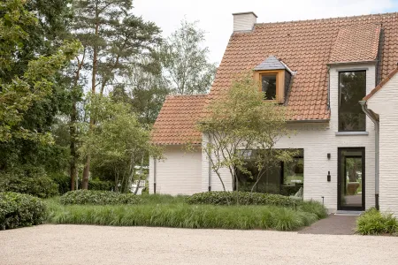 Witgekaleide villa met dakkapel en border van sierlijke pluimgrassen langs de grindoprit