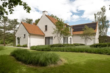 Witgekaleide hoevestijl villa met zonnepanelen, omringd door glooiend gazon en siergrassen