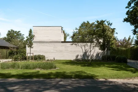 Zijgevel van een moderne villa in travertijn, omgeven door een strak grasveld en jonge boomaanplant in Keerbergen.