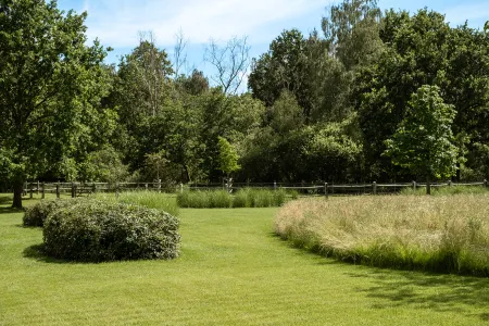 Kronkelend graspad tussen wuivende bloemenweides, met een houten poort in de verte.