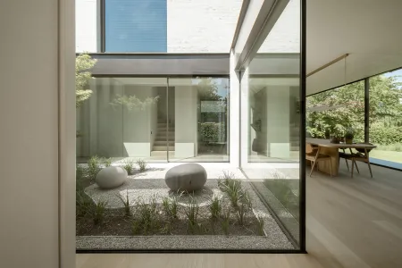 Minimalistische binnentuin met grind, ronde natuurstenen sculpturen en siergrassen, zichtbaar vanuit de eetruimte.