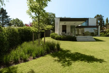 Overdekt terras met zwart uitkragend dak aan de achterzijde van de villa, met glooiend gazon in Keerbergen.