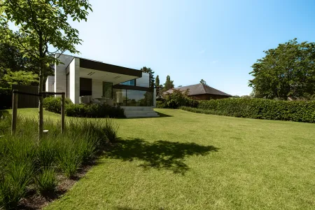 Weids gazon met haagrand, uitzicht op de moderne villa met zwart overkragend dak in Keerbergen.