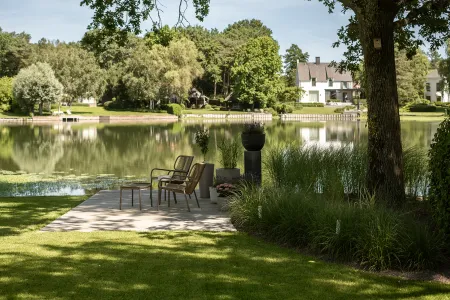Rotan loungestoelen op een houten vlonder aan de waterkant, omzoomd door siergrassen in de tuin in Keerbergen.
