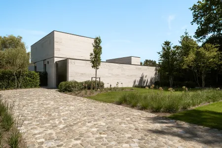 Kasseien oprit die kronkelt langs de travertijnen villa, met sierui en grassen in de border.