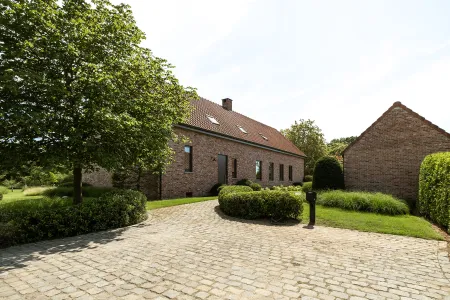 Kasseien oprit langs een rode bakstenen hoeve, omzoomd door bolvormige buxus en siergrassen in Westerlo.