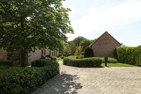 Kronkelende kasseioprit tussen hagen, met zicht op de bijgebouwen van de hoeve.