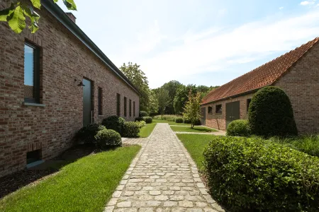Recht kasseipad tussen de hoofdwoning en het bijgebouw, met strak gesnoeide buxusbollen langs het gazon.