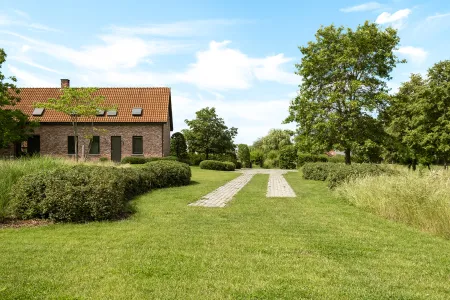 Graspad tussen gemengde hagen en siergrasborders, leidend naar de ingang van de hoeve.