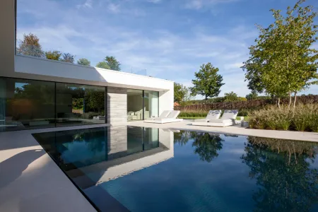 Witte villa met ligstoelen aan het zwembad.