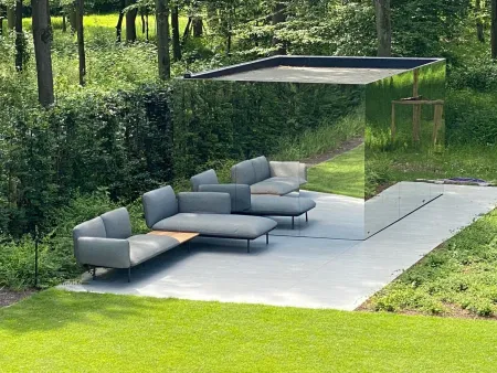 Terras bij een spiegelende tuinwand, met dicht bos op de achtergrond.