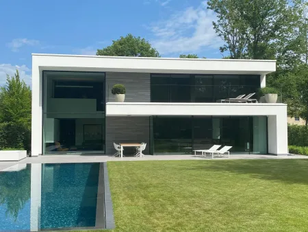 Achteraanzicht van witte villa met zwembad en groot gazon, omgeven door bos in Bonheiden.