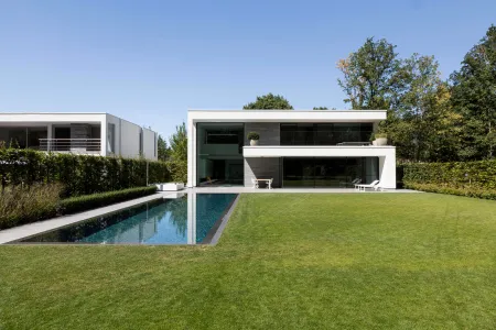 Strakke witte villa met lengtezwembad en groot gazon, omgeven door bos in Bonheiden.