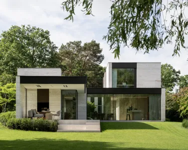 Achtergevel van een moderne villa in travertijn, omgeven door een strak grasveld in Keerbergen.